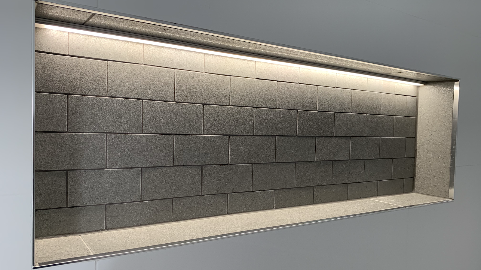 Wall niche lit by a hidden LED strip against dark tiles