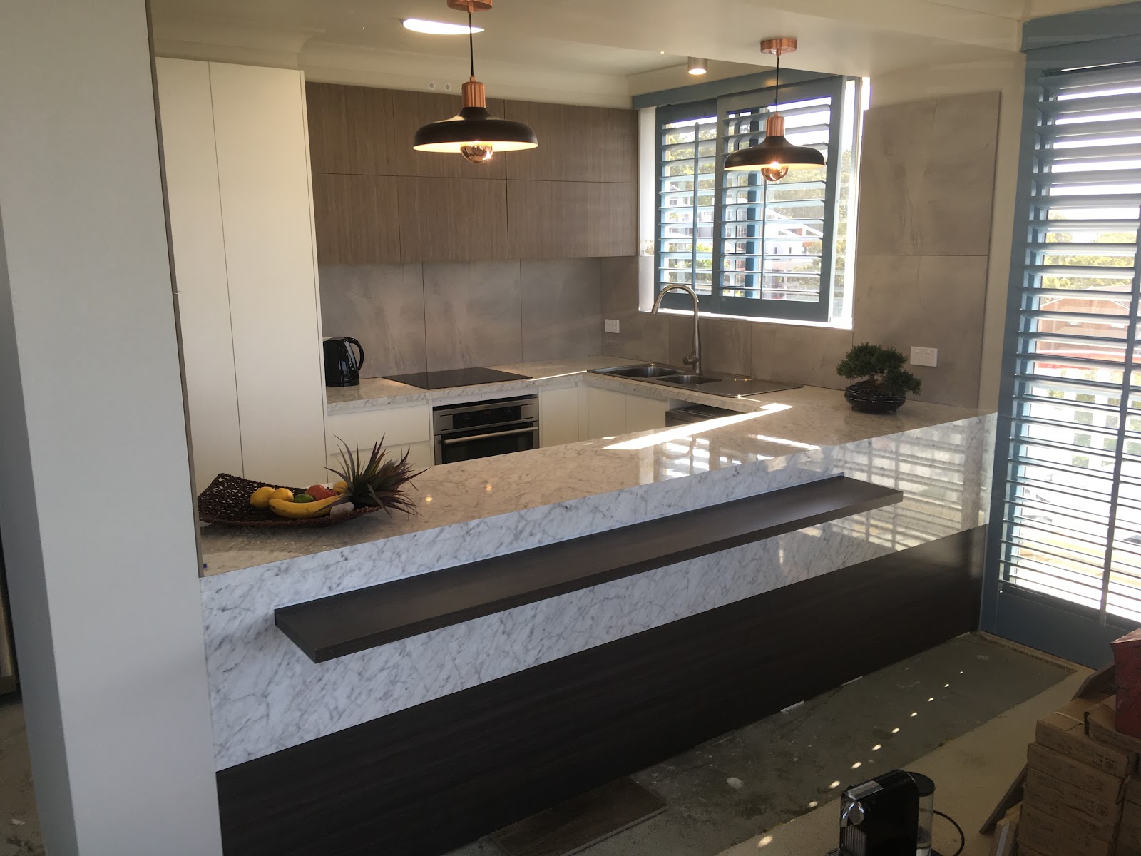 Renovated kitchen with copper pendants and downlights over a stone bench