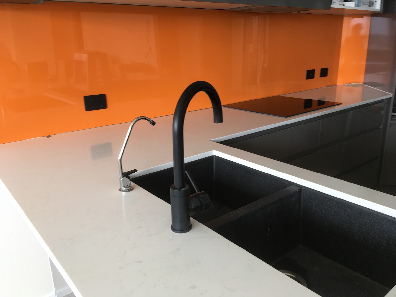 Kitchen with an orange glass splashback and power points above the bench