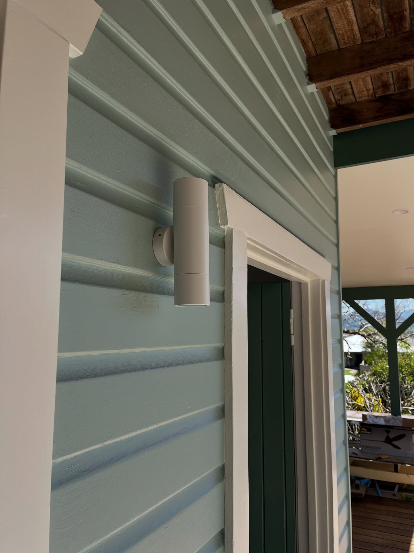 White cylinder wall light on a weatherboard wall beside a doorway