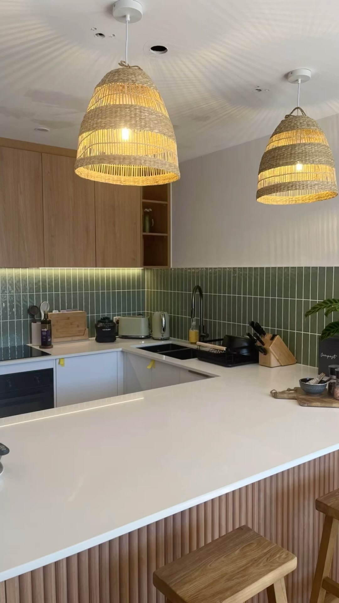 Kitchen with woven pendant lights above a white benchtop and green tiles